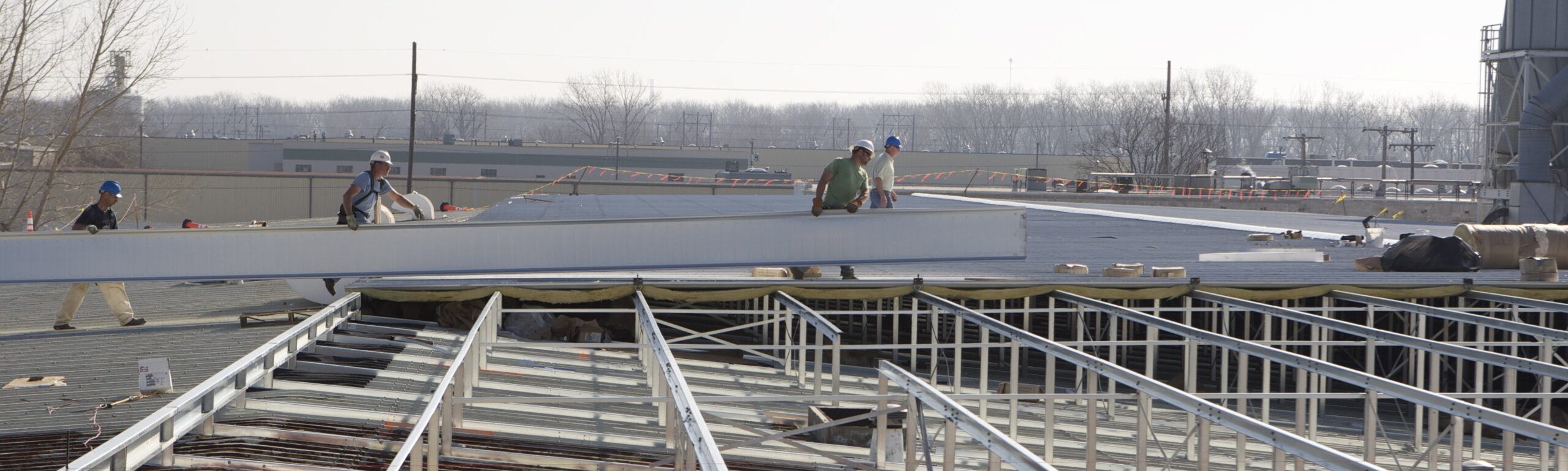 Construction crew positioning large insulated metal roof panels on a commercial building during reroof installation.